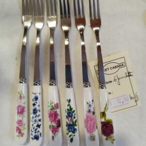 Row of eight forks with white floral-patterned handles laid out on a white surface; a price tag is nearby.