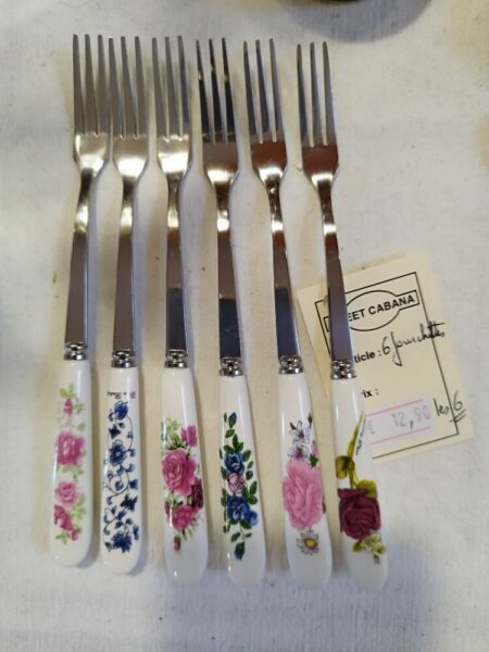 Row of eight forks with white floral-patterned handles laid out on a white surface; a price tag is nearby.